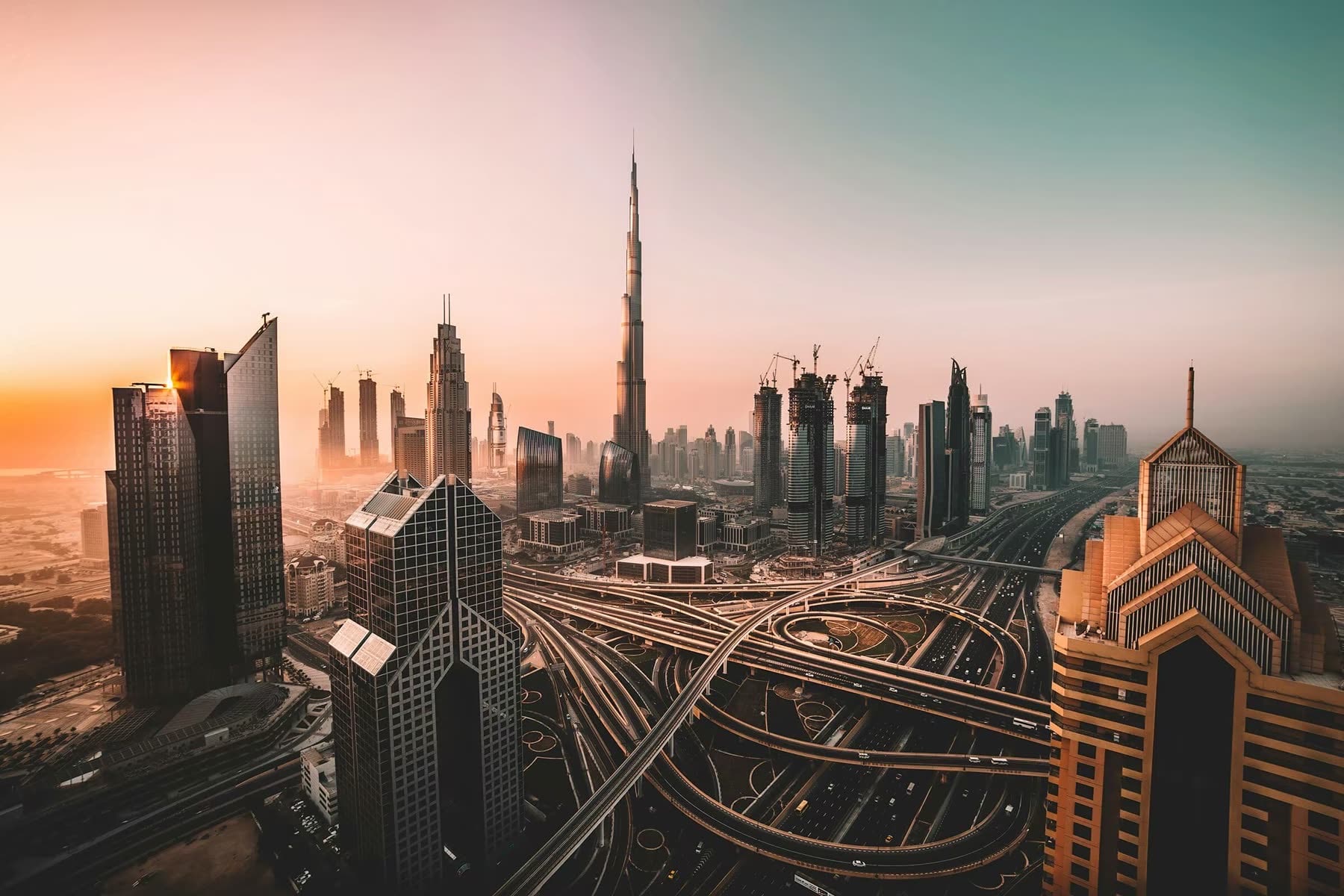 A city of towers at golden hour, its freeway interchanges winding between them.