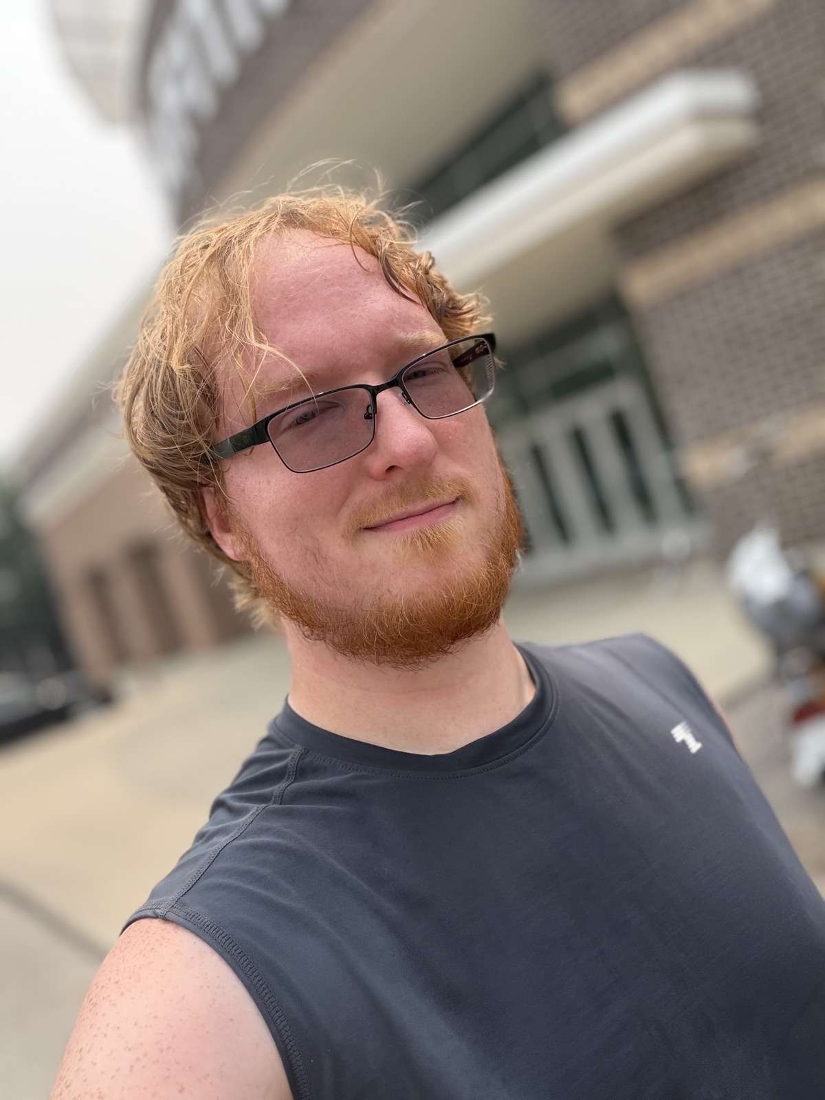 Justin K Kazmierczak, author of Exploit, in a sleeveless workout shirt outside the gym